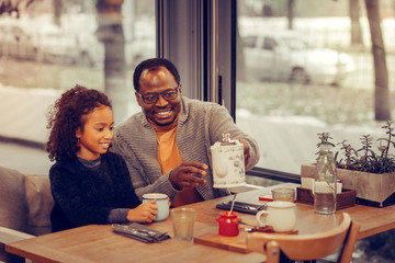 Curly daughter wearing sweater having breakfast with father