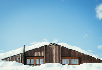 Modern wood house with windows and snow on the roof, blue sky with text space