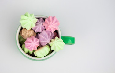 Green cup with meringues on a white background. French meringue dessert cooked with sugar and baked eggs. Copy space