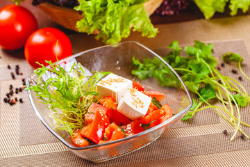 Salad with tomatoes, herbs and cheese in glass bowl