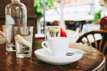 Closeup of a cup of coffee and some glasses on a wooden table in the morning with sunlight and relaxing in the free time. Photo of a moment of relax in the holiday with a hot beverage