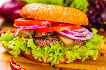 Hamburger with beef cutlet, tomatoes and onion rings on wooden cutting board