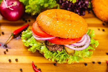 Hamburger with beef cutlet, tomatoes and onion rings on wooden cutting board