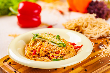 Noodles with vegetables and chicken in beige plate on wooden board