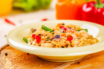 Pasta with seafood and vegetables in white plate on wooden cutting board