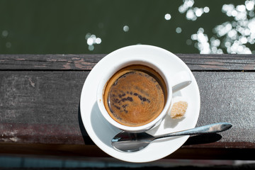 A small white porcelain espresso cup on a saucer with a teaspoon and two pieces of sugar