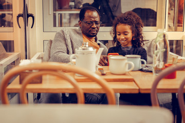 Father and daughter playing game on smartphone sitting in cafeteria
