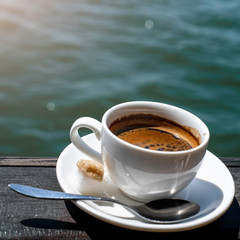 A small white porcelain espresso cup on a saucer with a teaspoon and two pieces of sugar