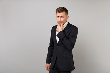Portrait of concerned young business man in classic black suit, shirt put hand prop up on chin isolated on grey background in studio. Achievement career wealth business concept. Mock up copy space.