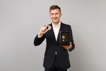 Smiling young business man in suit holding bitcoin, future currency, metal bank safe for money accumulation isolated on grey background. Achievement career wealth business concept. Mock up copy space.