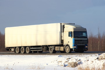 European white semi-trailer truck with logo copy space for writing on winter road on forest trees and blue sky background - side front view