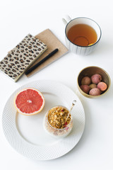 Fototapeta na wymiar Healthy business Breakfast. Ingredients: grapefruit, granola, yogurt, lychee, tea. Diaries on the table. Side view, white background.