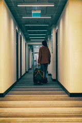 Unrecognizable girl back to us goes down the hall of the hotel with a travel bag