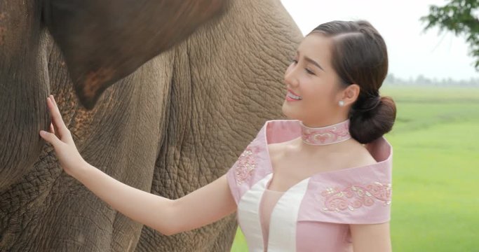 Tenderness of young attractive asian woman in traditional costume with elephant. Concept: love of animals, softness, and nature.