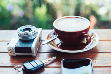 Cup of hot coffee , film camera smartphone and key on the wood plate