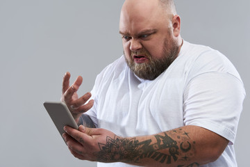 Close up of bold bearded man feeling angry with his smartphone