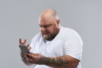 Close up of bearded man feeling angry and looking at smartphone