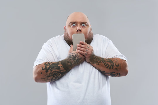 Scared Fat Man Putting Smartphone To His Mouth And Opening Eyes Wide