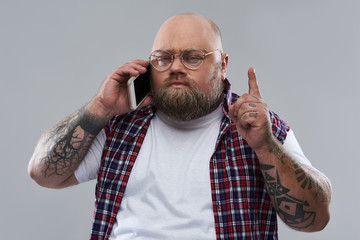 Thoughtful bearded man pointing his finger up while talking on the phone