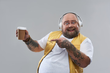 Waist up of positive fat man pointing to the cup of coffee and smiling