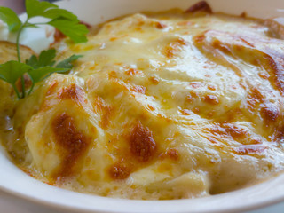 Sorrentinos con queso muzzarella gratinado decorado con hoja verde de perejil en plato ondo de pasta color blanco