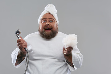 Waist up of excited man smiling and holding shower head and shower puff