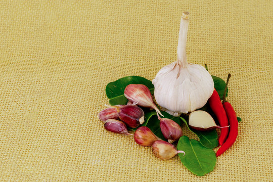 garlic whole head bulb denticle red chile pepper chili leaves lime on a yellow leaf background