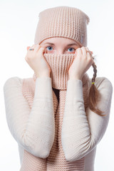 A girl with blue eyes and pigtails hides her face behind a knitted scarf. Slightly scared look