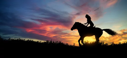 Wandcirkels Paardrijden Silhouet van een vrouw bij een paard bij zonsondergang  © ginettigino
