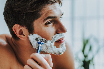 Attractive guy shaving his beard by razor