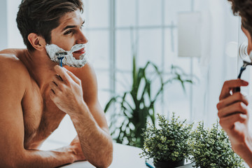 Smiling guy shaving his beard by razor