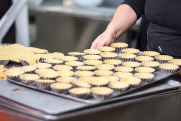 Pastry chef making tartlets, putting the dough in baking dishes, at kitchen of pastry shop .