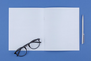 Fototapeta premium school notebook with pen and glasses on a blue table