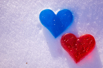 Two hearts are red and blue in the snow. Handmade soap in the shape of a heart. Love and valentines day concept. Romantic background with free space for text.