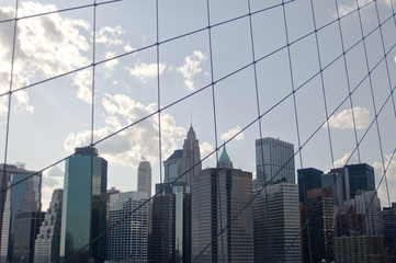 Fototapeta na wymiar A cluster of buildings situated in New York City's lower Manhattan as seen through the high-tension wires of the iconic Brooklyn Bridge.