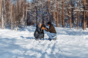 A happy couple with a dog (black Labrador) having fun outside in the forest on a sunny frosty winer day.