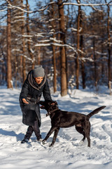 A happy woman with a dog (black Labrador) having fun outside in the forest on a sunny frosty winer day.