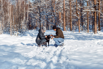 A happy couple with a dog (black Labrador) having fun outside in the forest on a sunny frosty winer day.