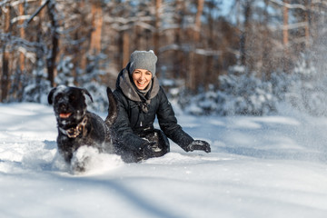 Fototapeta na wymiar A happy woman with a dog (black Labrador) having fun outside in the forest on a sunny frosty winer day.
