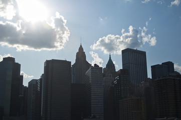 Fototapeta premium A shadowy silhouette of the cluster of buildings and structures at New York City's lower Manhattan set against cloudy blue sky.