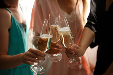 Women party or happy birthday party. Close-up view of sexy, young girls clinking glasses of champagne on hen-party before the wedding day, at home. Dressed in silk nightclothes.