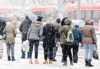 People waiting for public transport at bus stop in heavy blizzard in winter