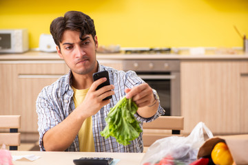 Young man calculating expences for vegetables in kitchen 