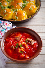 Soup borscht made with vegetables, meat, beans and beet root in a bowl and buns pampushky - bread rolls with garlic and parsley