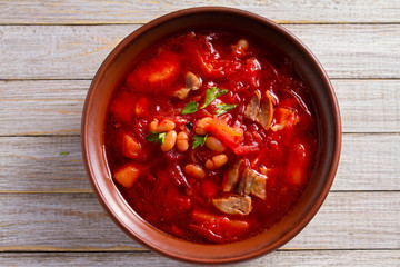 Soup borscht made with vegetables, meat, beans and beet root in bowl on wooden table
