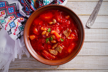 Soup borscht made with vegetables, meat, beans and beet root in bowl on wooden table