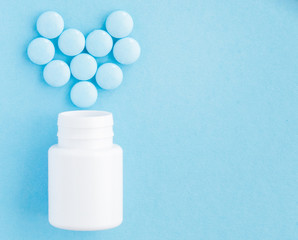 Pills heart out of pill bottle on blue background, top view
