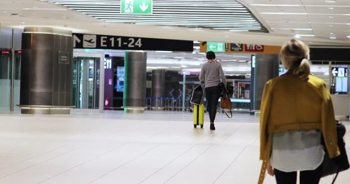 Female tourists with their bags and suitcases walking inside the airport. Back view.