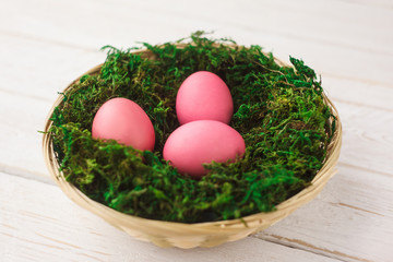 Easter eggs in a basket, a nest with moss on a white wooden background. Spring. selective focus