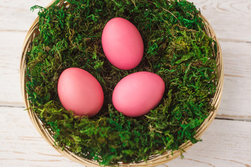 Easter eggs in a basket, a nest with moss on a white wooden background. Spring. selective focus